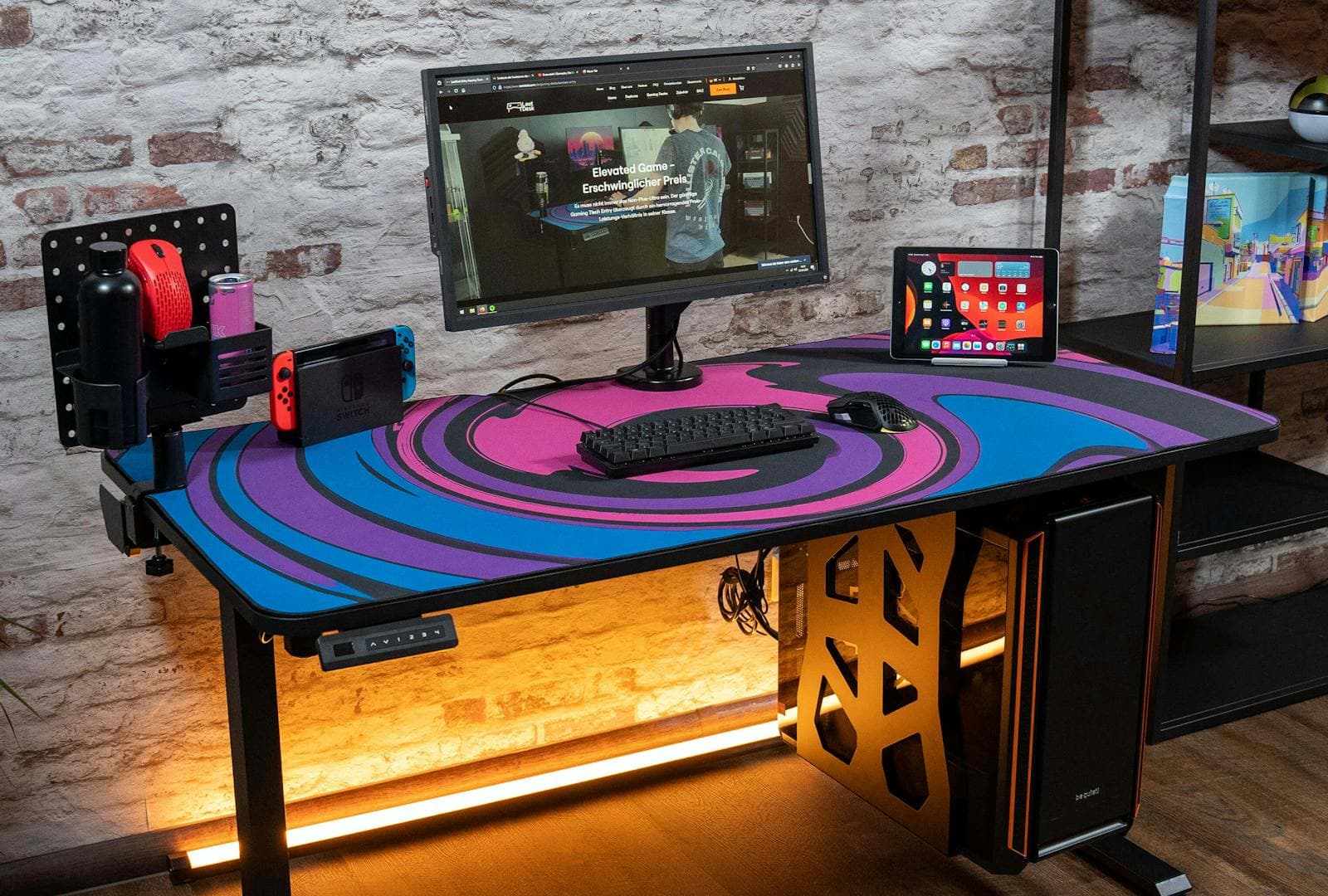 A black deskpad with a colorful swirl pattern on a height-adjustable Leetdesk, featuring dual mousepads rolled up on the tabletop. The mauspad covers a large portion of the desk surface for optimal use.