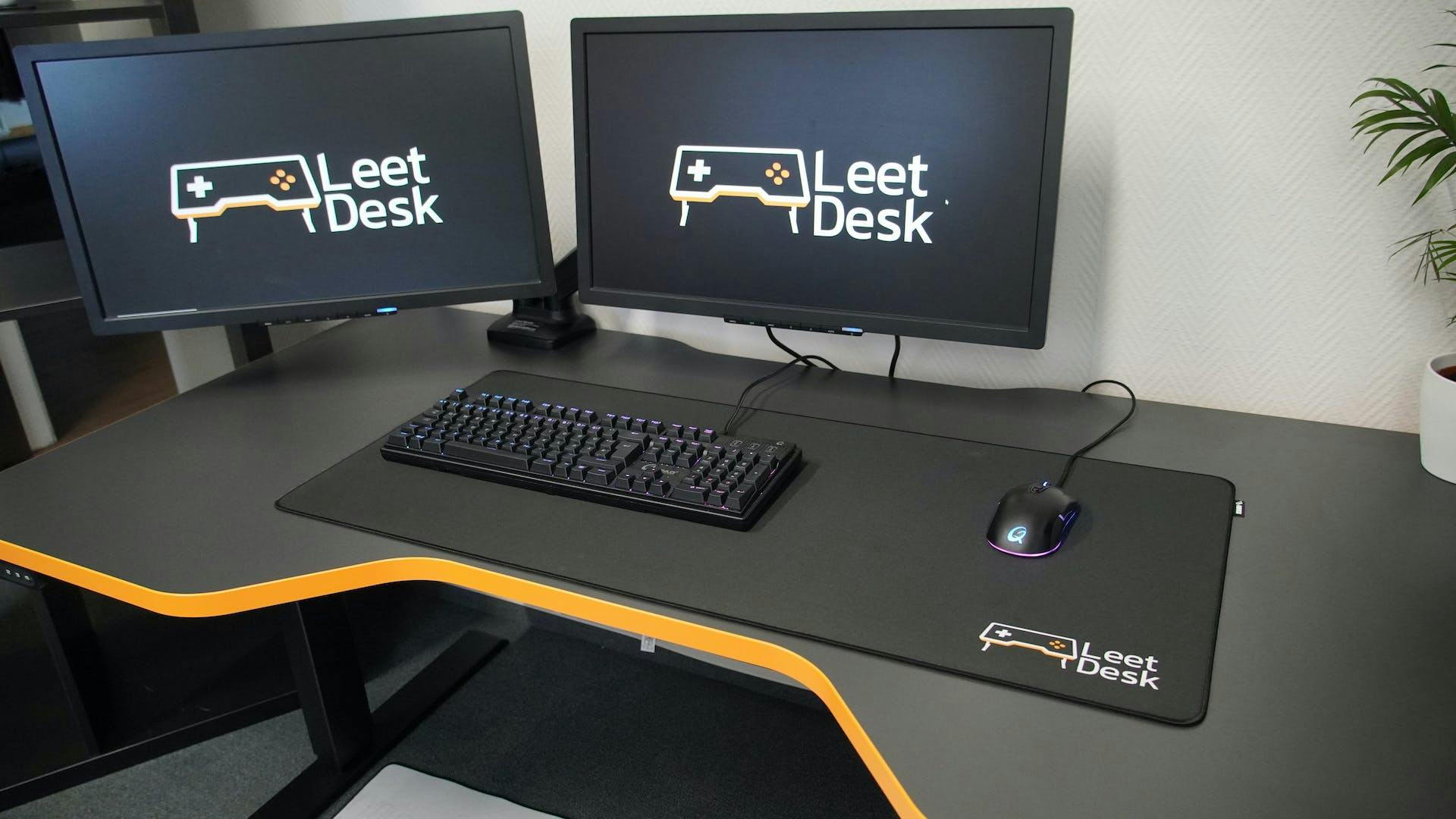 Auf einem Gaming Tisch von LeetDesk mit zwei Gaming Monitoren liegt ein großes Mauspad, dass einen Großteil des Tisches einnimmt, auf dem sowohl Gaming Tatatur als auch Gaming Maus Platz finden